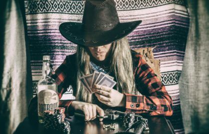 Old west cowgirl gunslinger sitting at table playing poker